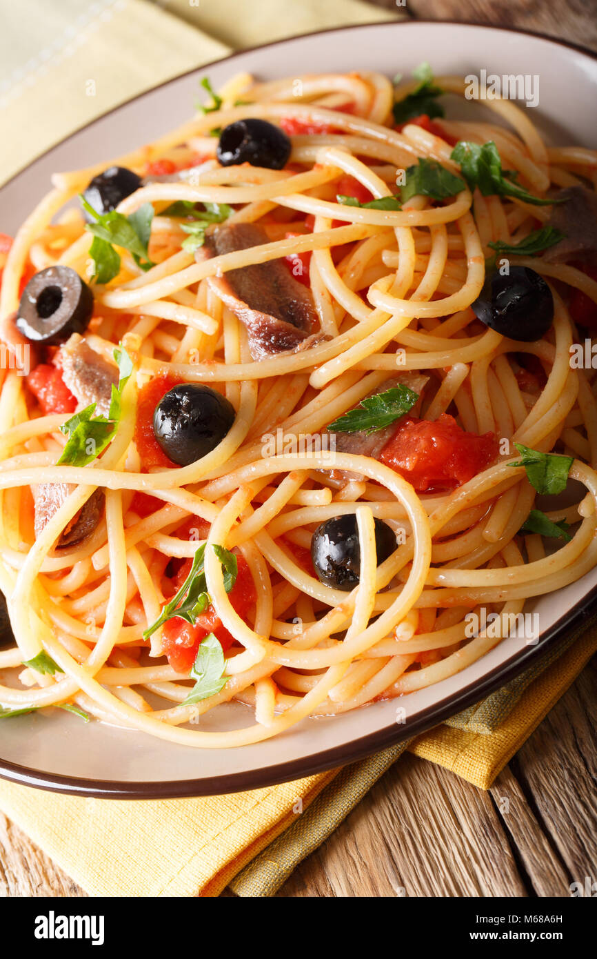 Italienische Pasta alla Puttanesca mit Sardellen, Tomaten, Knoblauch und schwarzen Oliven Makro auf einem Teller. Vertikale Stockfoto