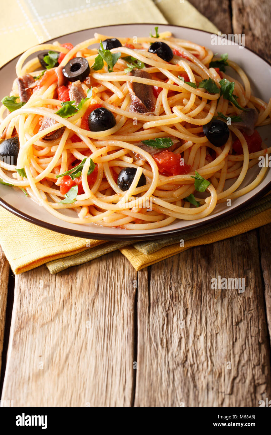Traditionelle Pasta alla puttanesca mit Sardellen, Tomaten, Knoblauch und schwarzen Oliven close-up auf einem Teller auf den Tisch. Vertikale Stockfoto