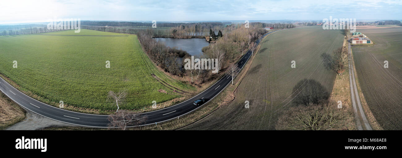 Composite Panorama von Luftaufnahmen und Luftaufnahmen von einer geraden Straße neben einem Teich und einem Feld, abstrakte Wirkung durch Verzerrung aufgrund der Stockfoto