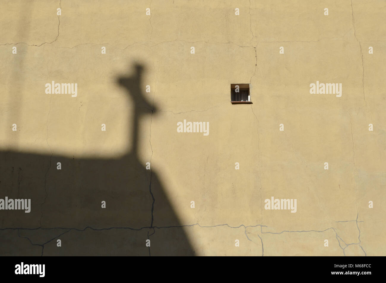 Schatten des Kreuzes aus einem nahe gelegenen Kirche auf eine Wand mit einem kleinen Fenster in Madrid. Stockfoto Schatten des Kreuzes aus einem nahe gelegenen Kirche auf eine Wand mit einem kleinen Fenster in Madrid. Stockfoto