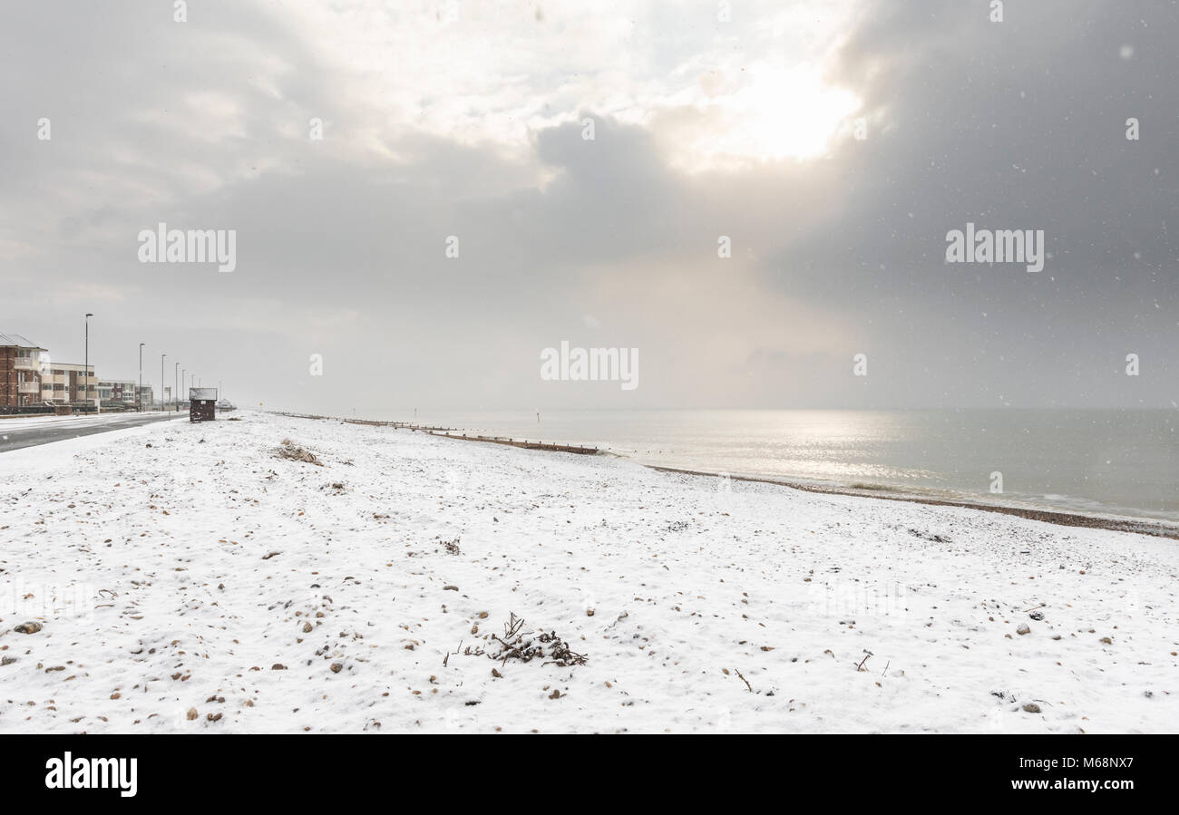 Schnee auf einem verlassenen Strand mit der aufgehenden Sonne obwohl Wolken im Winter in Littlehampton, West Sussex, England, UK. Stockfoto