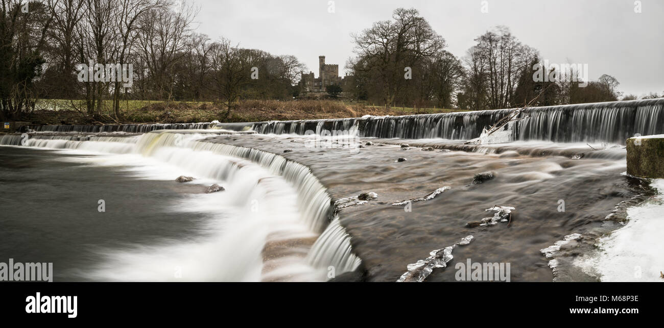 Wier auf dem Fluss Wenning mit Hornby Schloss darüber hinaus an einem kalten, eisigen Tag. Stockfoto