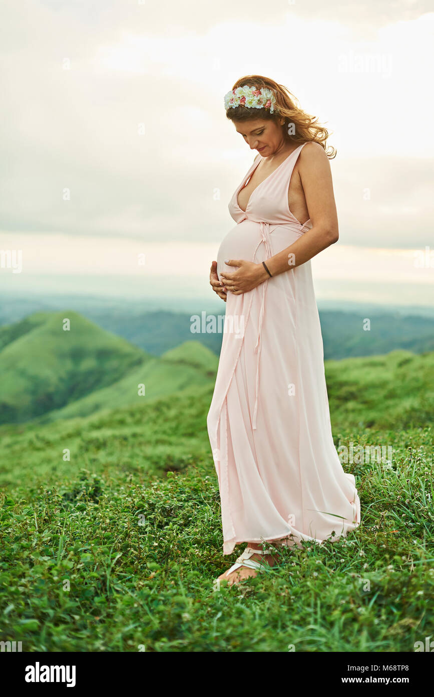 Schwangere Frau stand auf Gras und Hände auf Bauch Stockfoto