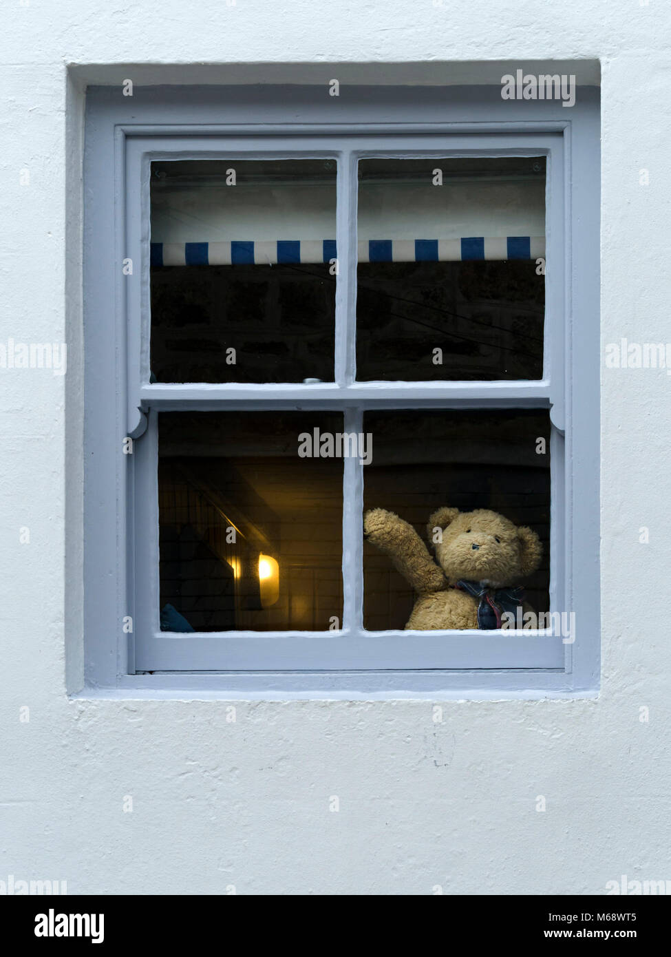 Der süße Teddybär winkt Hallo oder verabschiedet sich vom Hausfenster, was auf Selbstisolation oder soziale Distanzierung während der Corona-Virus-Kovid19-Pandemie hindeutet Stockfoto