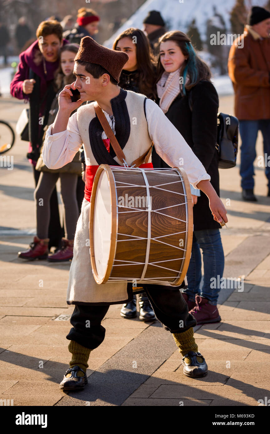 PERNIK, Bulgarien - 26. JANUAR 2018: die männlichen Schlagzeuger in der bulgarischen Folklore Kostüm spricht über das Mobiltelefon während Drumming in sonnigen Wintertag am annua Stockfoto