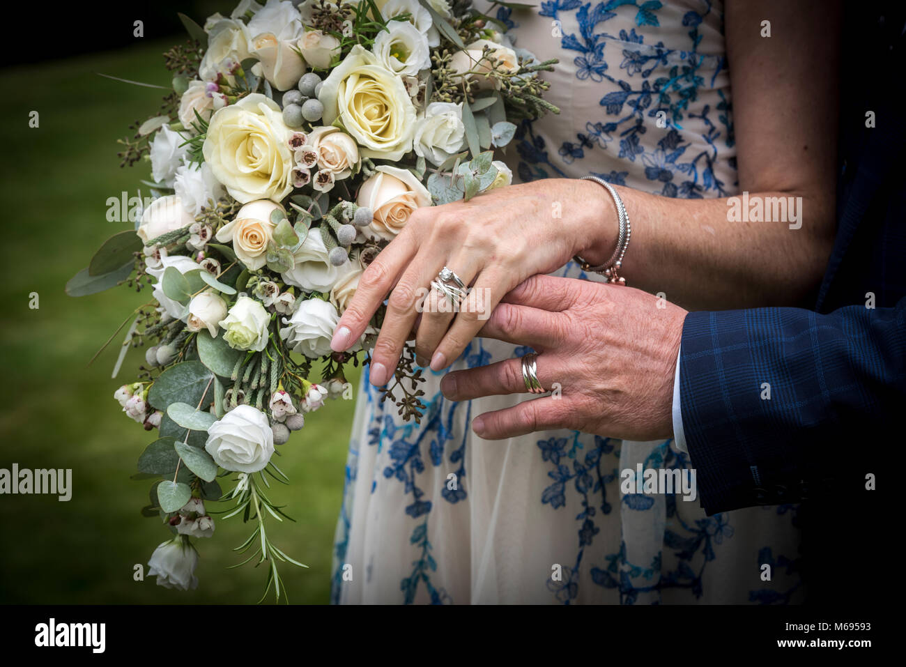 Hand der Ehe für sie und ihn Trauringe vor einem Blumenstrauß Stockfoto