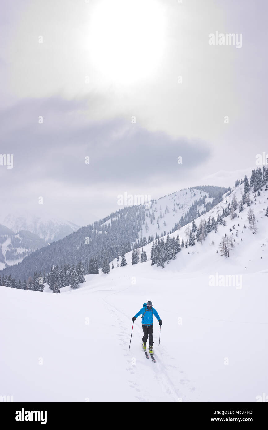 Ski Bergsteiger aufsteigend einen schneebedeckten Berg, auf kalten Wintertag bedeckte sein Gesicht warm eingepackt. Pulverschnee im Hinterland von Österreich. Stockfoto