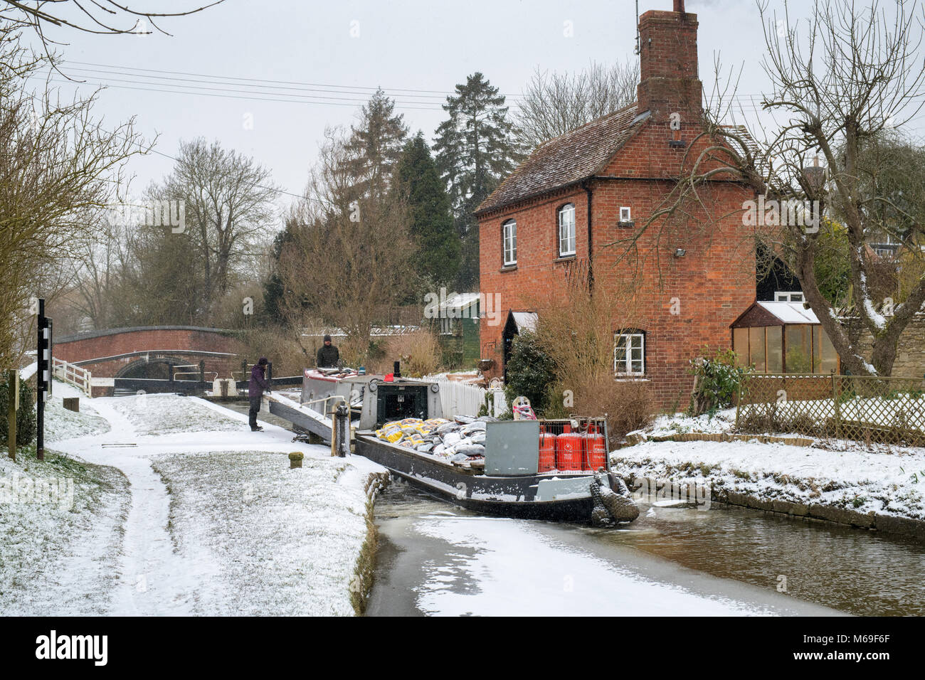 Der Lastkahn durch die Schleuse kommen neben dem Lock Keepers Cottage im Winter Schnee. Cropredy, Oxfordshire, England Stockfoto