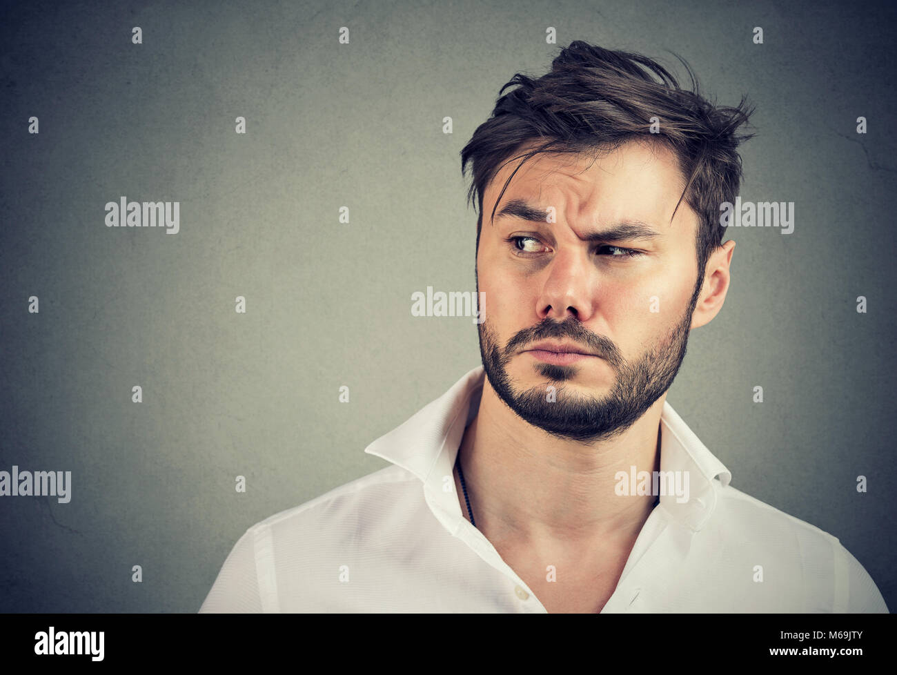 Gut aussehender bärtiger Mann im weißen Hemd weg schauen mit Verdacht auf grauem Hintergrund. Stockfoto