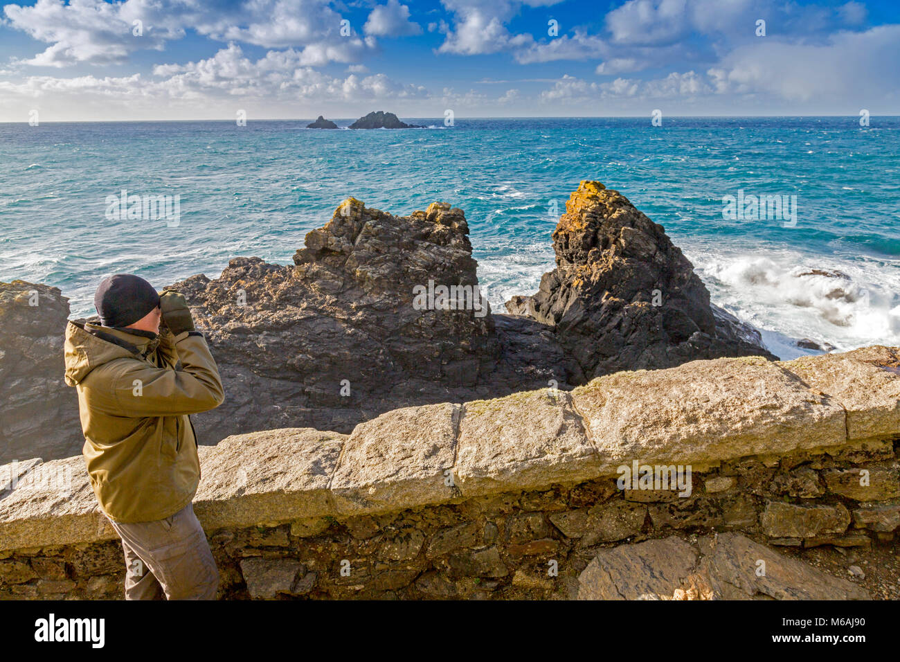 Ein vogelbeobachter auf dem South West Coast Path am Cape Cornwall mit der Brisons Felsen über, England, Großbritannien Stockfoto