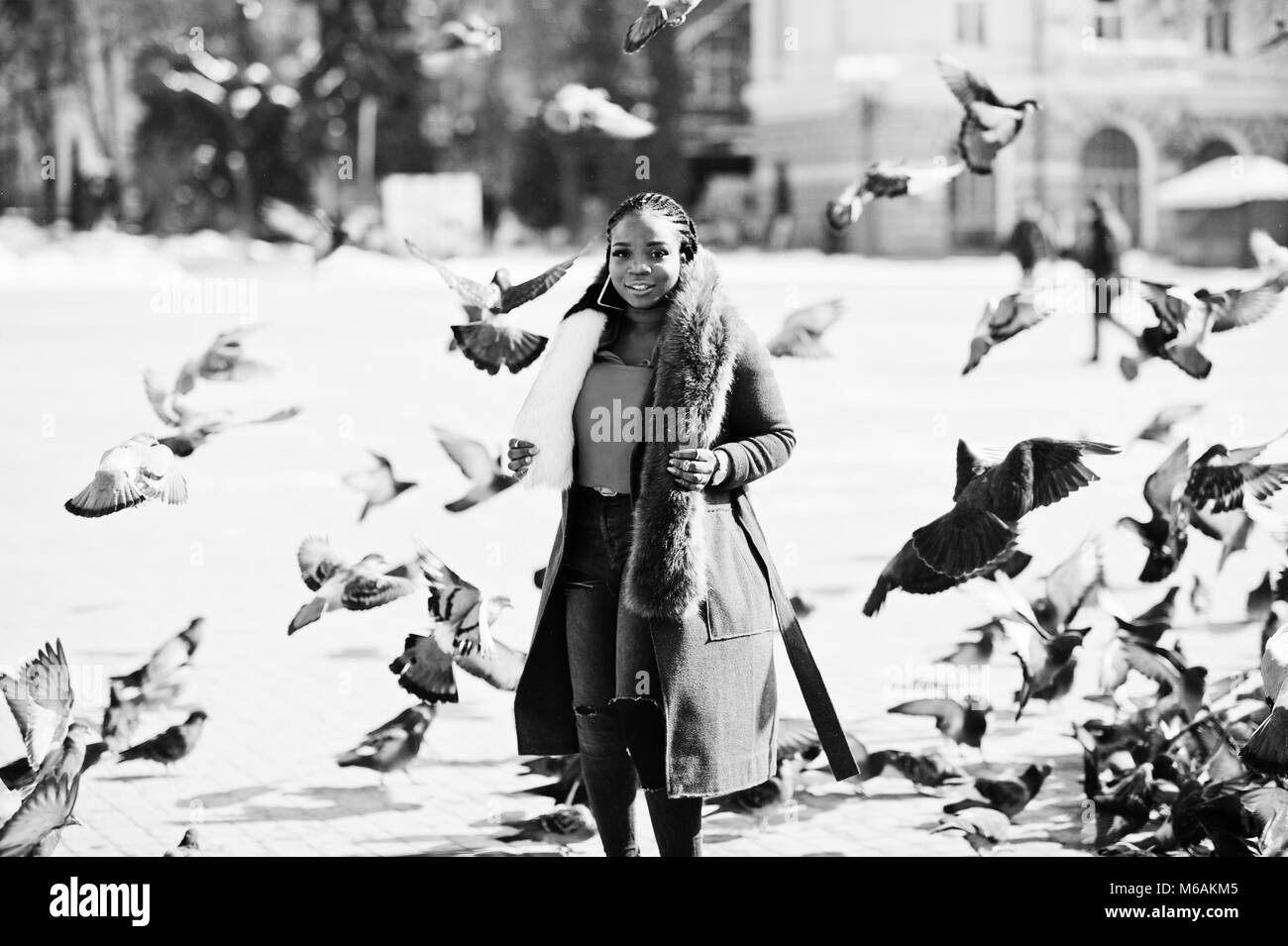 Reichen afrikanischen amerikanischen Mädchen im roten Mantel und Fell gegen Masse von piqeons. Schwarz elegante Frau. Stockfoto