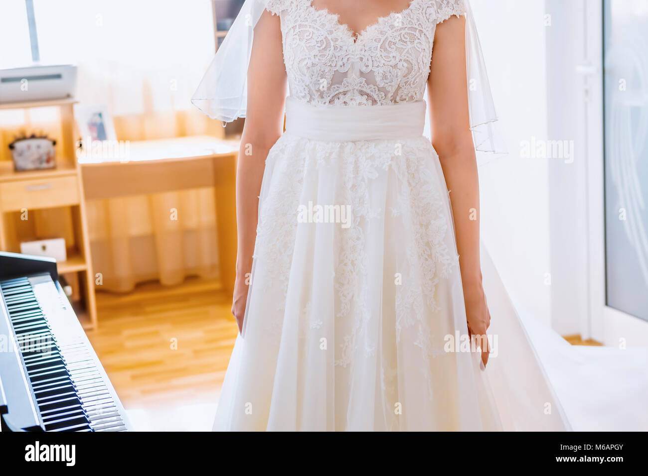 Braut im weißen Kleid neben Klavier im Wohnzimmer. Fokus auf Kleid! Stockfoto
