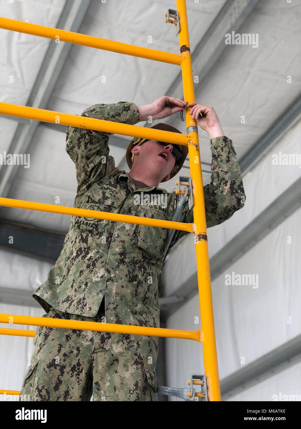 Builder Constructioman Andrew Dempsey, eine Seabee zu Naval Mobile Konstruktion Bataillon (NMCB) 11, hilft montieren Gerüste für Rollup Tür Installation im alpha Vorgefertigte Gebäude zugeordnet. NMCB 11 ist in Gulfport, Mississippi homeported, und ist Teil des Schiffsbaus Kraft (NCF). Sie haben derzeit Mitarbeiter an mehr als 15 Standorten Welt zugeordnet, eine Vielzahl von Missionen zur Unterstützung der Marine und das Verteidigungsministerium. Stockfoto