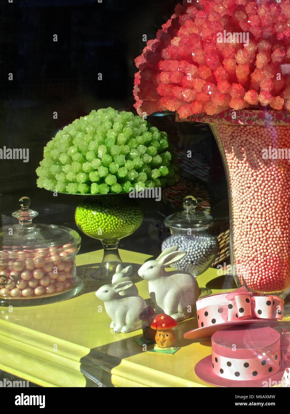 Rosa und grün Bonbons mit Porzellan Kaninchen und rosa Hüte auf einem gelben Tabelle in einer Ostern Süßigkeiten. Stockfoto