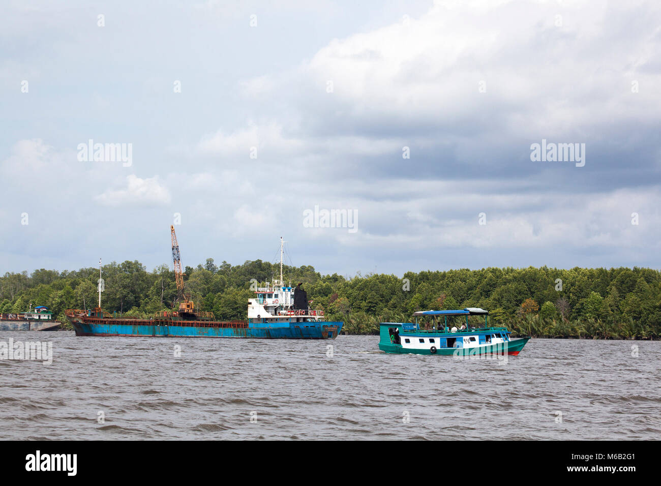 Ein Industrieboot und ein kleineres Klotok, ein traditionelles Flussboot, auf dem Kumai River, das den Hafen von Kumai im Zentrum von Kalimantan, Indonesien verlässt Stockfoto
