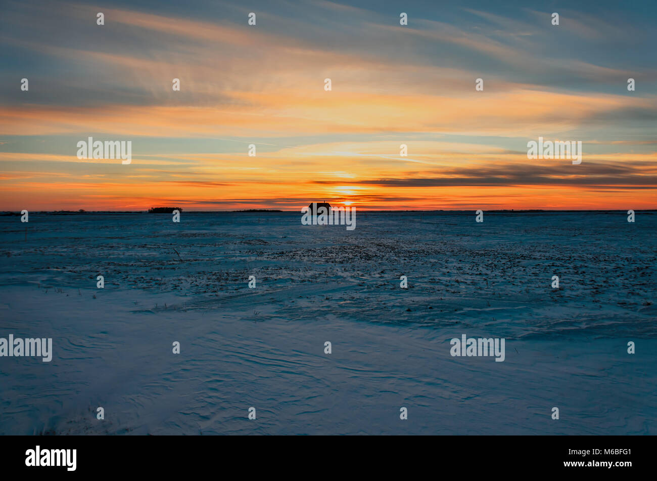 Riesige blaue Himmel in rosa Wolken bei Sonnenuntergang der Tag, eine orange rot Glühen von der Sonne über einem schneebedeckten Feld mit einem schwarzen Silhouette einer Hütte und einem gr Stockfoto