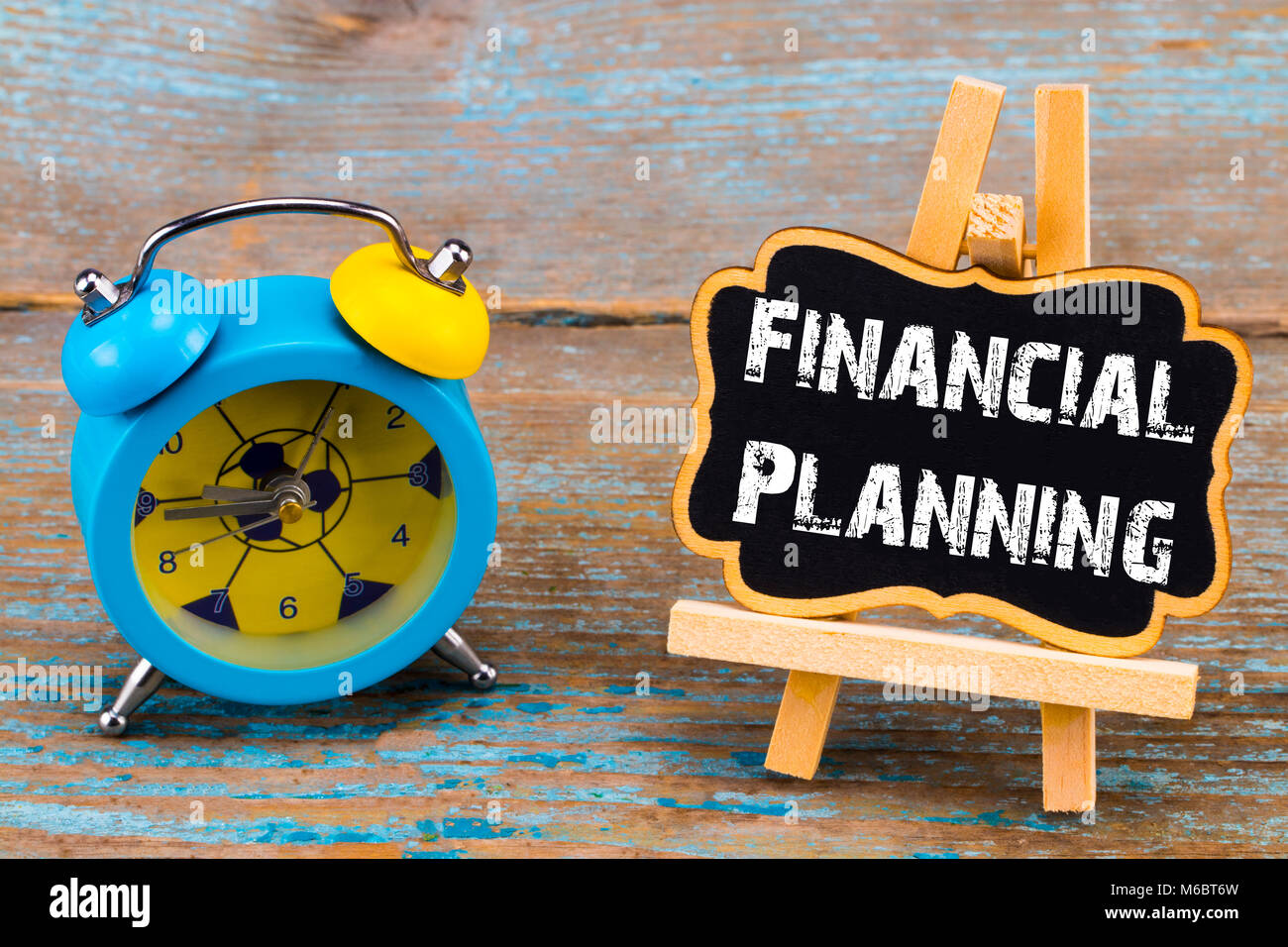 Wecker und eine Tafel mit dem Text - Finanzielle planningб, auf Holz- Hintergrund. Stockfoto