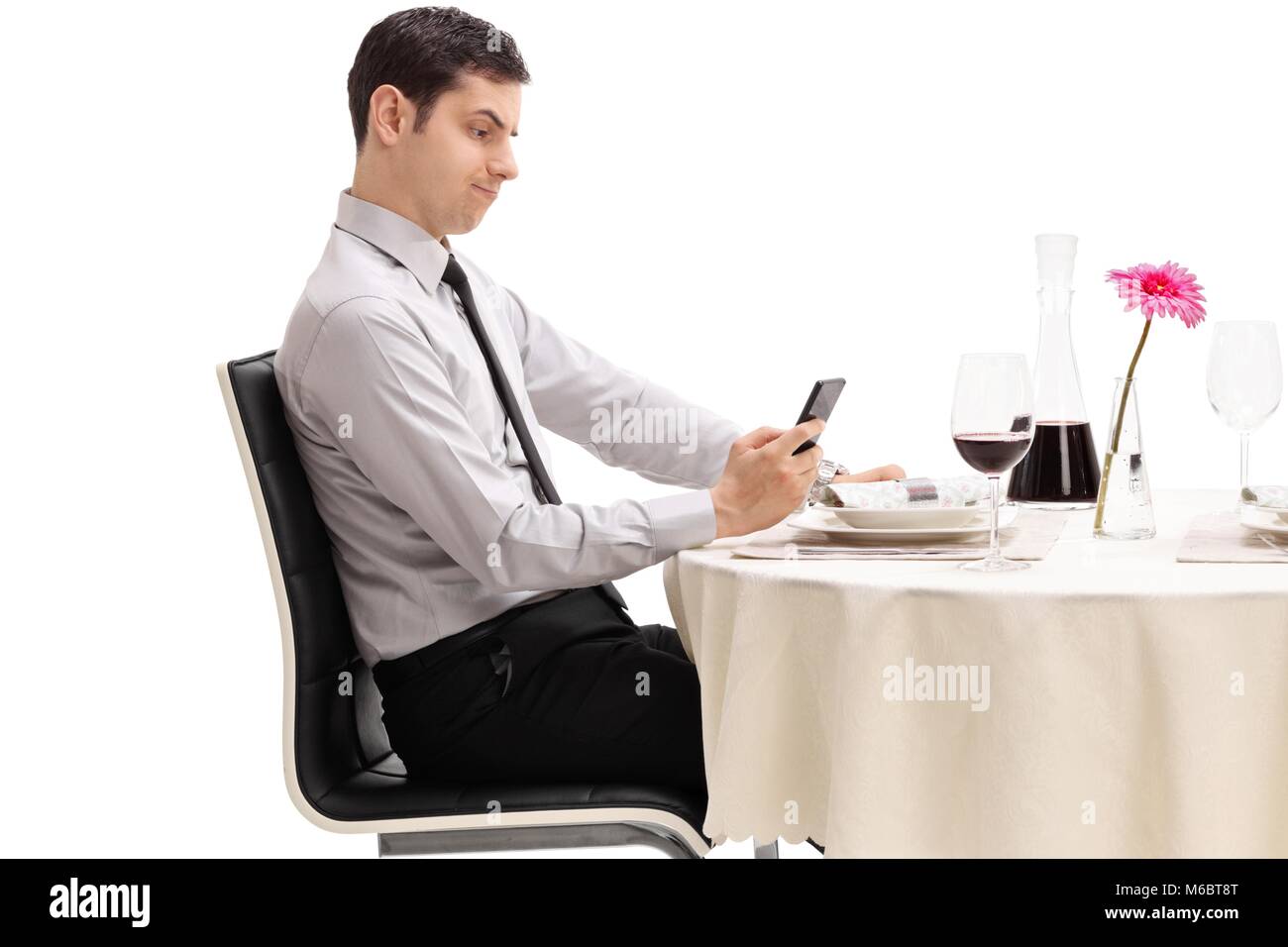 Enttäuscht junge Mann an einem Tisch im Restaurant sitzt an seinem Telefon auf weißem Hintergrund suchen Stockfoto