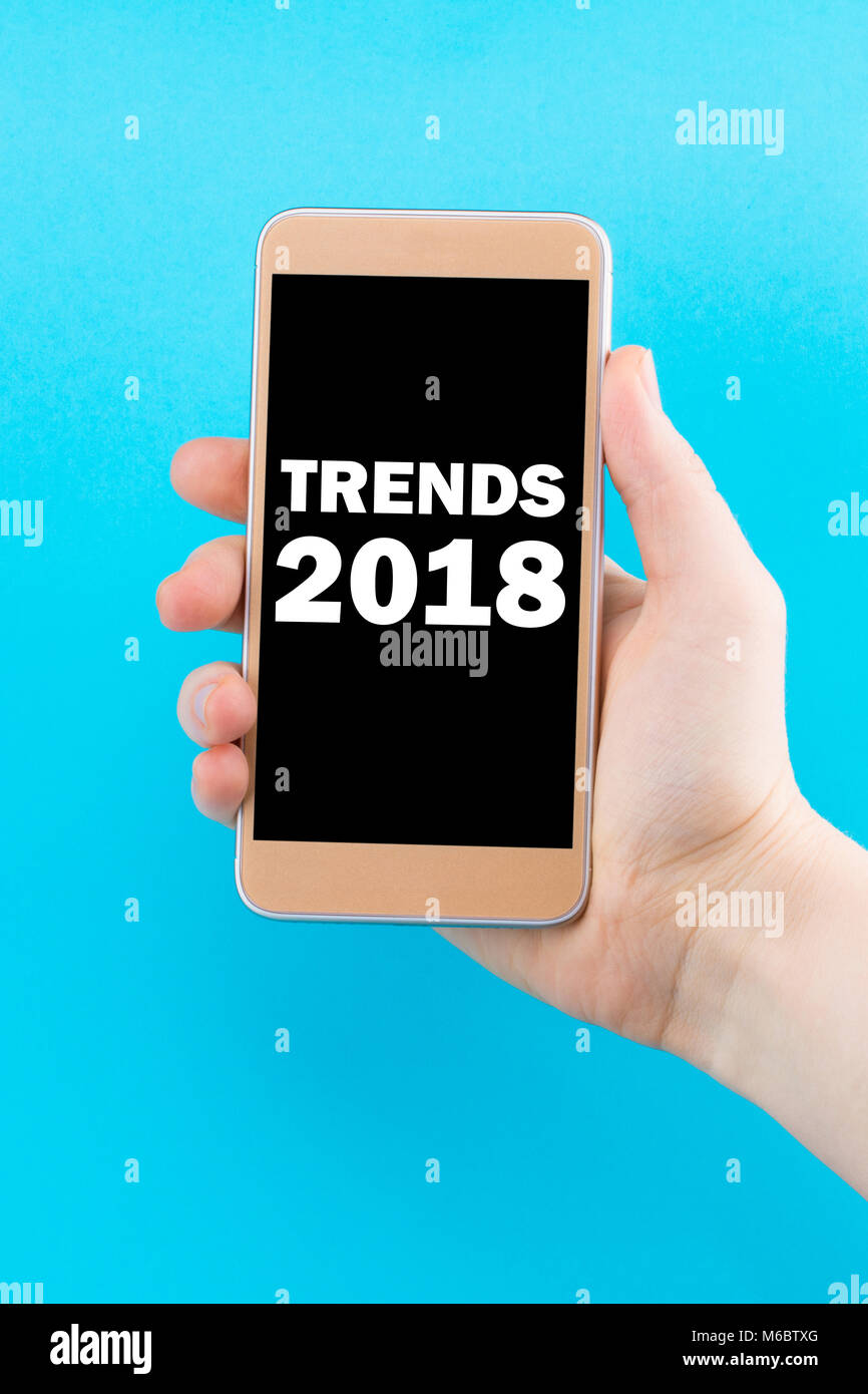 Trends 2018 Inschrift auf dem Telefondisplay. Golden Telefon in der Hand auf einem blauen Hintergrund. Stockfoto