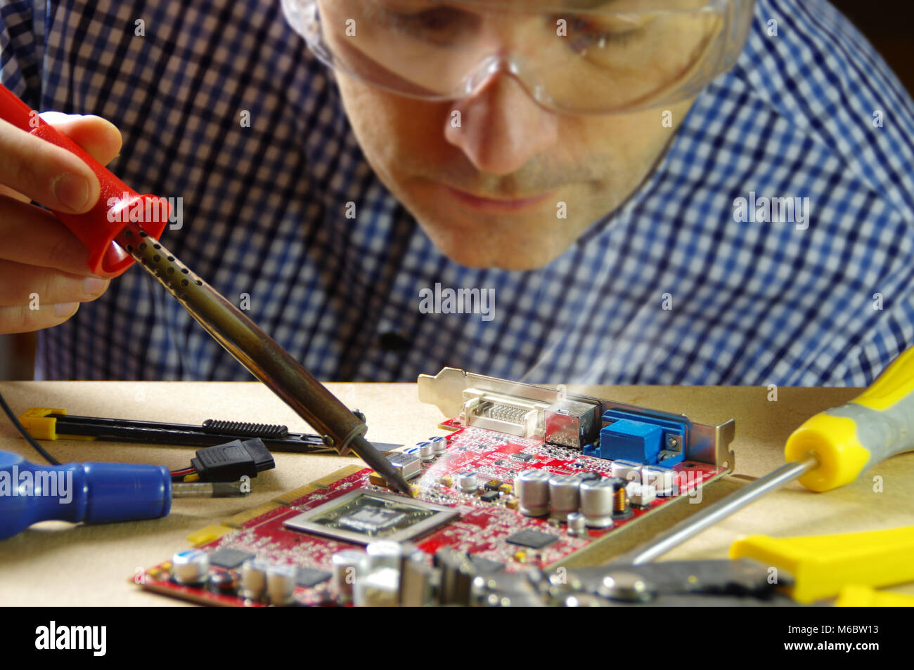 Techniker konzentrierte sich auf die Reparatur von elektronischen Geräten. Ein Mann bei der Arbeit mit einem Lötkolben. Stockfoto
