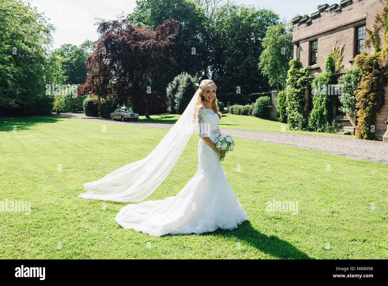 Schöne Braut posiert für die Kamera in ihrem Hochzeit Kleid in einem formalen Garten. Stockfoto