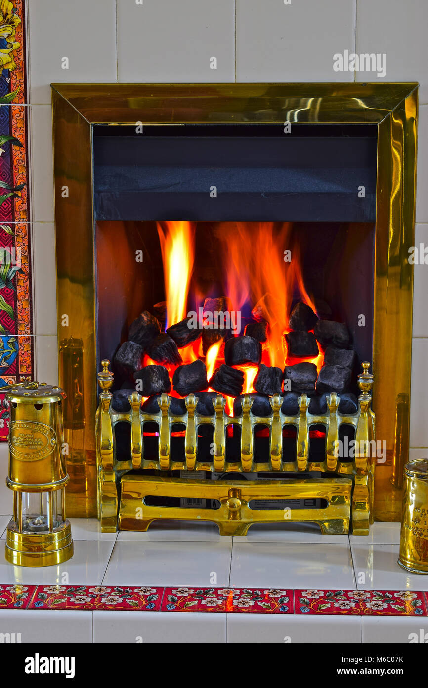 Gemütliche Kohle-Effekt gas Brand in Messing umgeben und mit einem Messing Miners Lamp. Das Feuer erzeugt eine warme und einladende Atmosphäre innerhalb des Hauses. Stockfoto