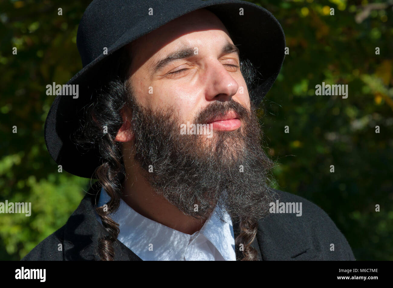 Außenbereich sonnige helle Porträt einer jungen orthodoxen jüdischen Mann mit Augen mit schwarzen Bart, Hut und Kostüm geschlossen Stockfoto