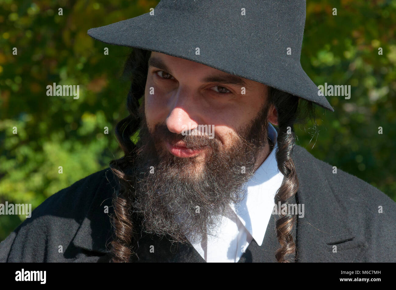 Außenbereich sonnige Porträt eines lächelnden suchen Jungen orthodoxen jüdischen Mann mit schwarzen Bart und Hut Stockfoto