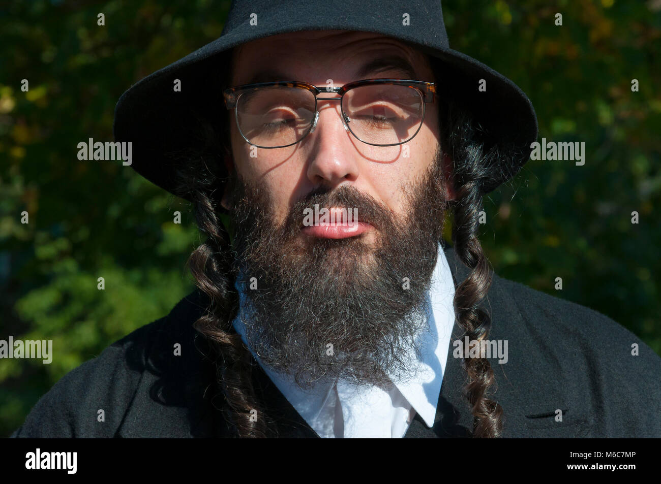 Außenbereich sonnige Portrait von verwirrten geschlossenen Augen jungen traditionellen orthodoxen jüdischen Mann mit schwarzen Bart und Hut Brille tragen Stockfoto