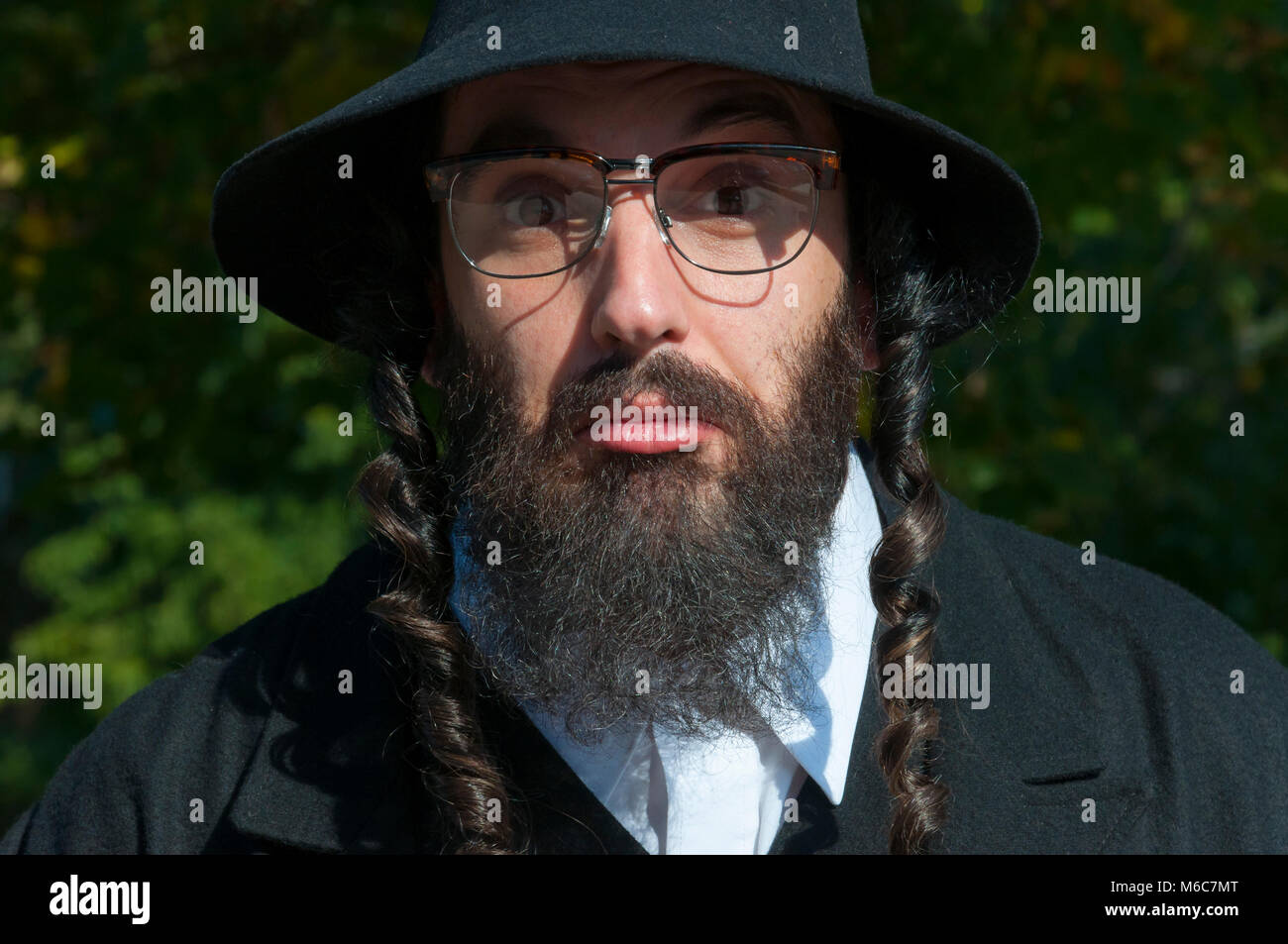 Außenbereich sonnige Portrait von verwirrten jungen seltsam aussehenden orthodoxen jüdischen Mann mit schwarzen Bart und Hut Brille tragen Stockfoto