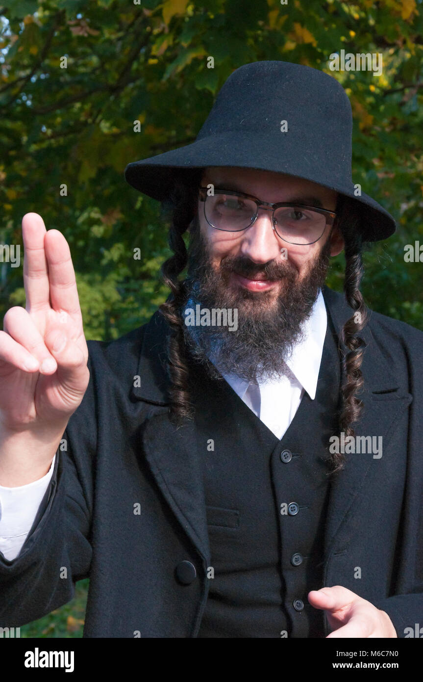 Sonnige Porträt einer jungen lächelnd glücklich Finger Segen traditionellen orthodoxen jüdischen Mann mit schwarzen Bart und Hut Brille tragen Stockfoto