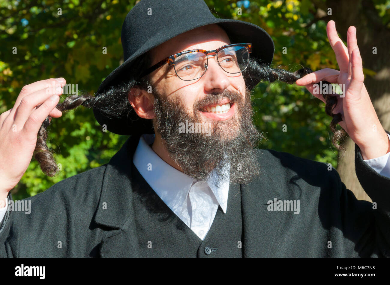 Außenbereich sonnige Porträt einer jungen glücklich orthodoxen jüdischen Mann mit Brille und schwarzen Bart holding Payot, sidelocks und bis in den Himmel suchen Stockfoto