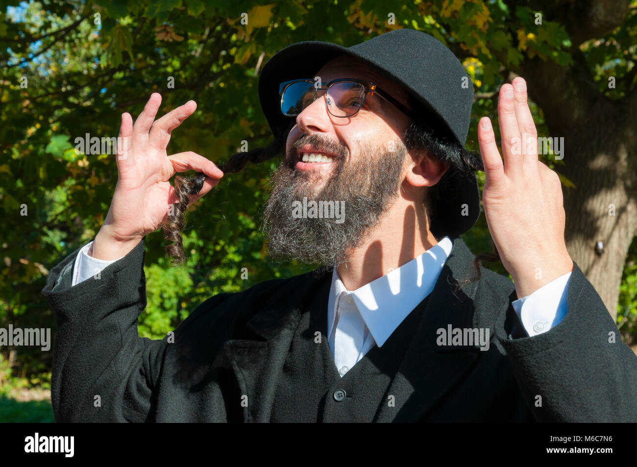 Außenbereich sonnige Porträt einer jungen glücklich orthodoxen jüdischen Mann mit Brille und schwarzen Bart holding Payot, sidelocks und bis in den Himmel suchen Stockfoto
