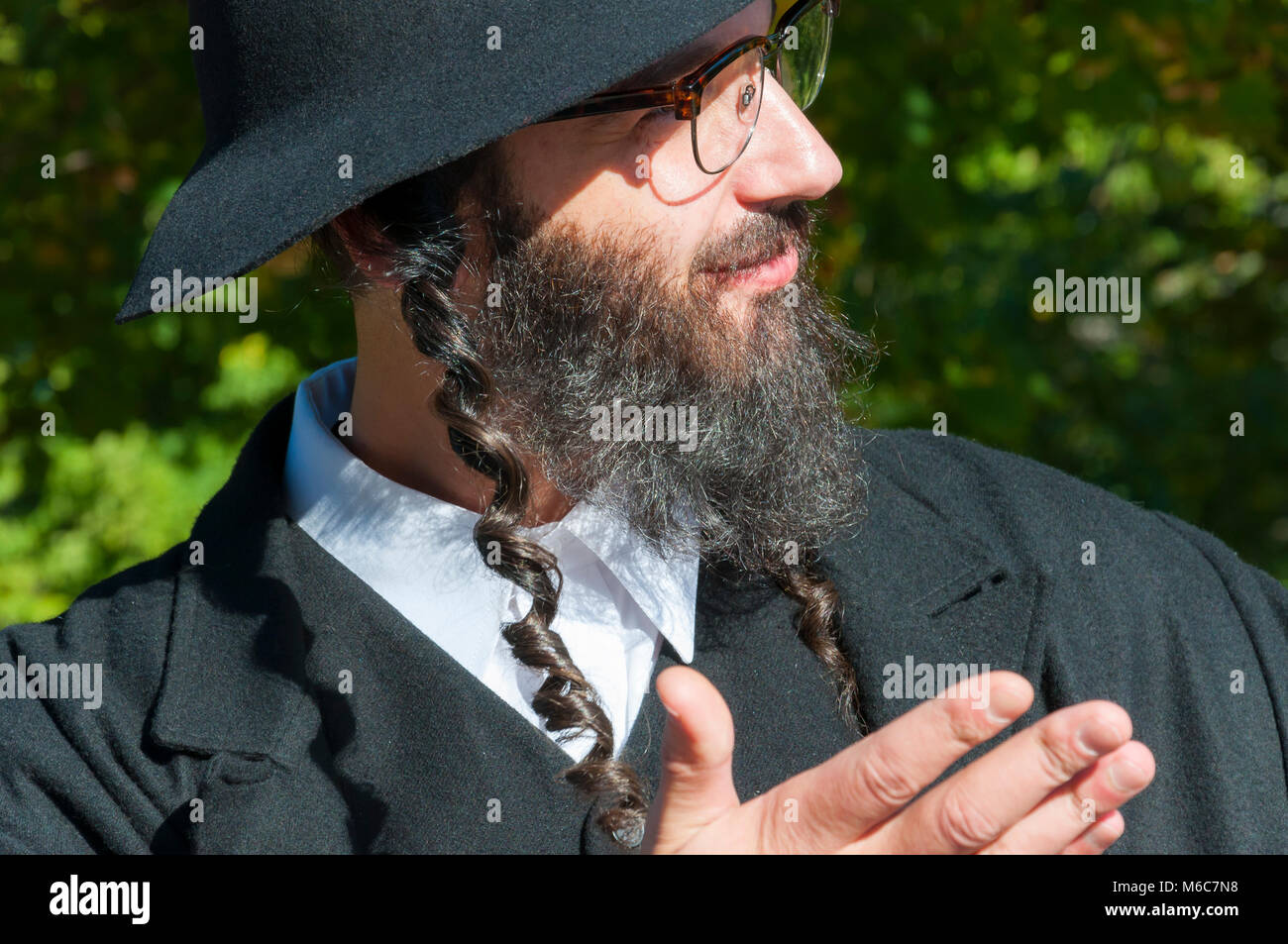 Außenbereich sonnige Porträt einer jungen gerne Beten traditionellen orthodoxen jüdischen Mann mit Brille und schwarzen Bart, Hut und Kostüm Stockfoto