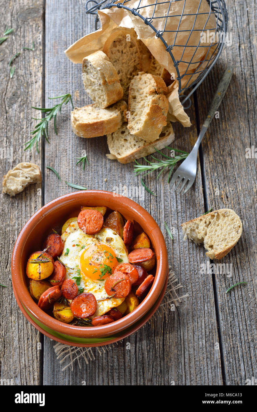 Spanische Tapa: Würzig Chorizo Wurst mit Spiegelei und Kartoffeln in einem Terra Cotta cazuela Gericht serviert. Stockfoto