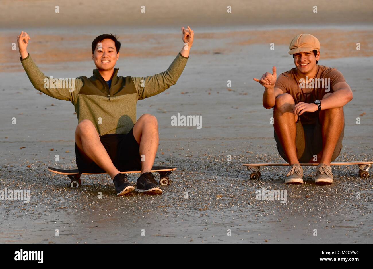 Zwei hip, junge Männer sitzen auf skateboards beobachten Sonnenuntergang am Strand, die Haka' Zeichen (chill out), in San Diego, Kalifornien, USA Stockfoto