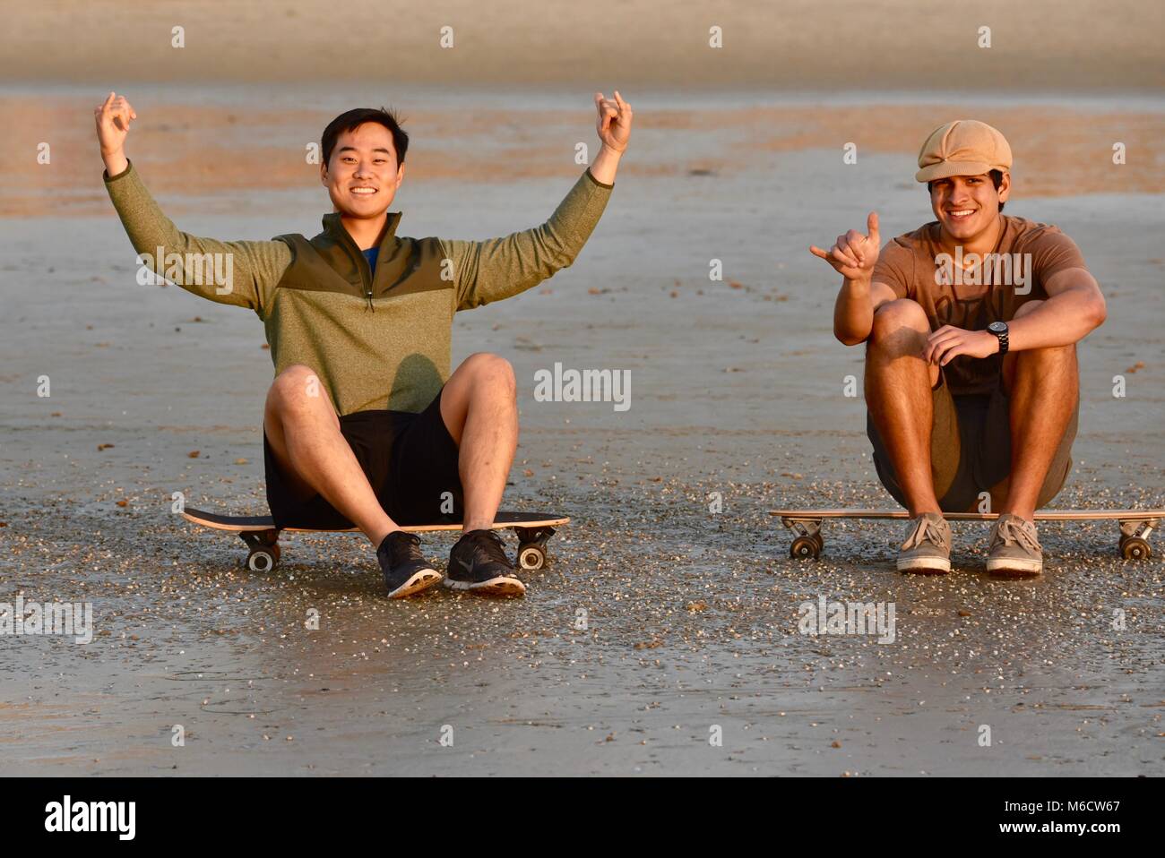 Zwei hip, junge Männer sitzen auf skateboards beobachten Sonnenuntergang am Strand, die Haka' Zeichen (chill out), in San Diego, Kalifornien, USA Stockfoto