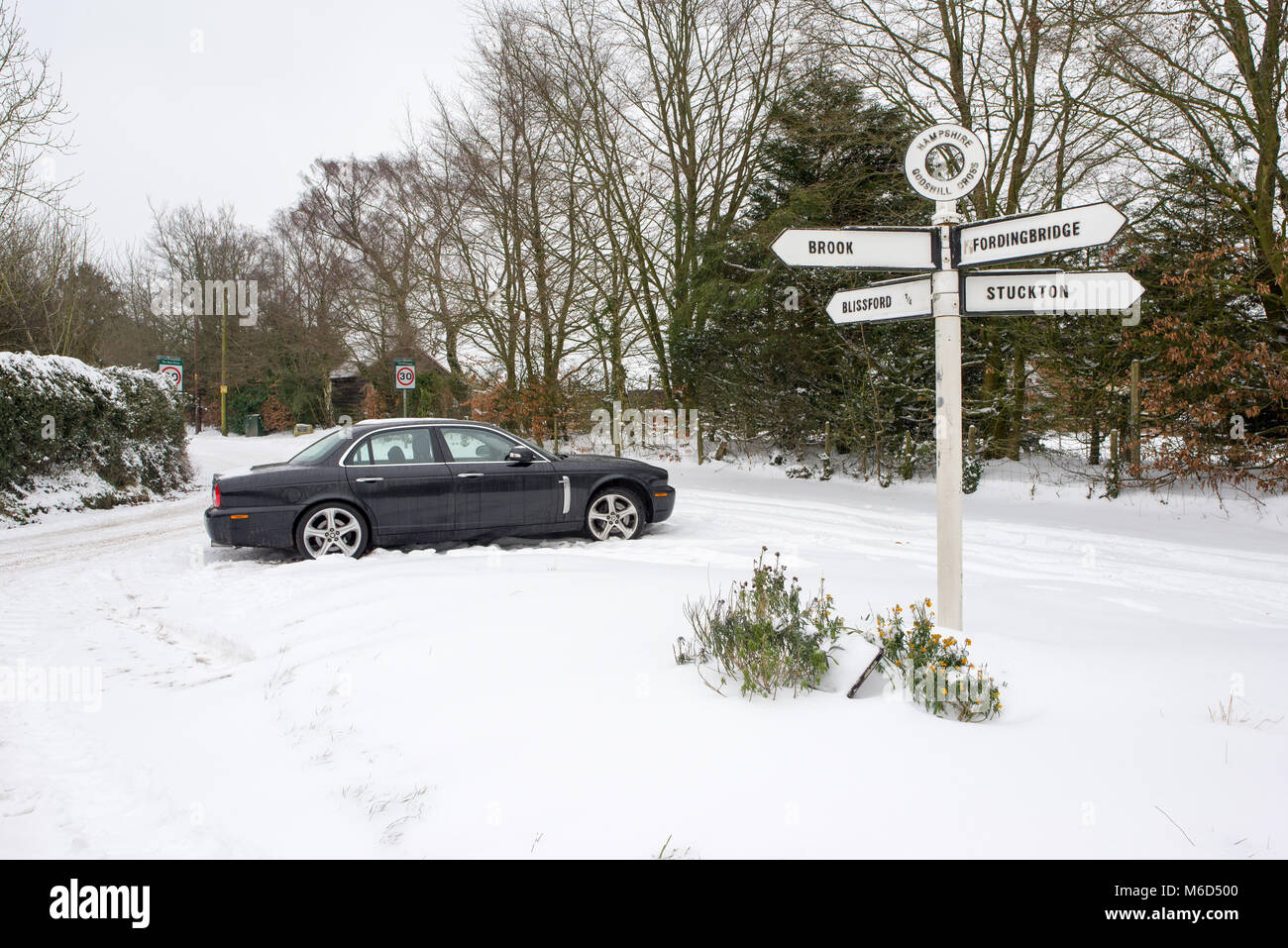 Jaguar Auto in der Nähe eines 4-polig Wegweiser an der Spitze eines Hügels im Schnee geparkten nach Sturm Emma, Godshill, New Forest, Hampshire, England, Großbritannien Stockfoto