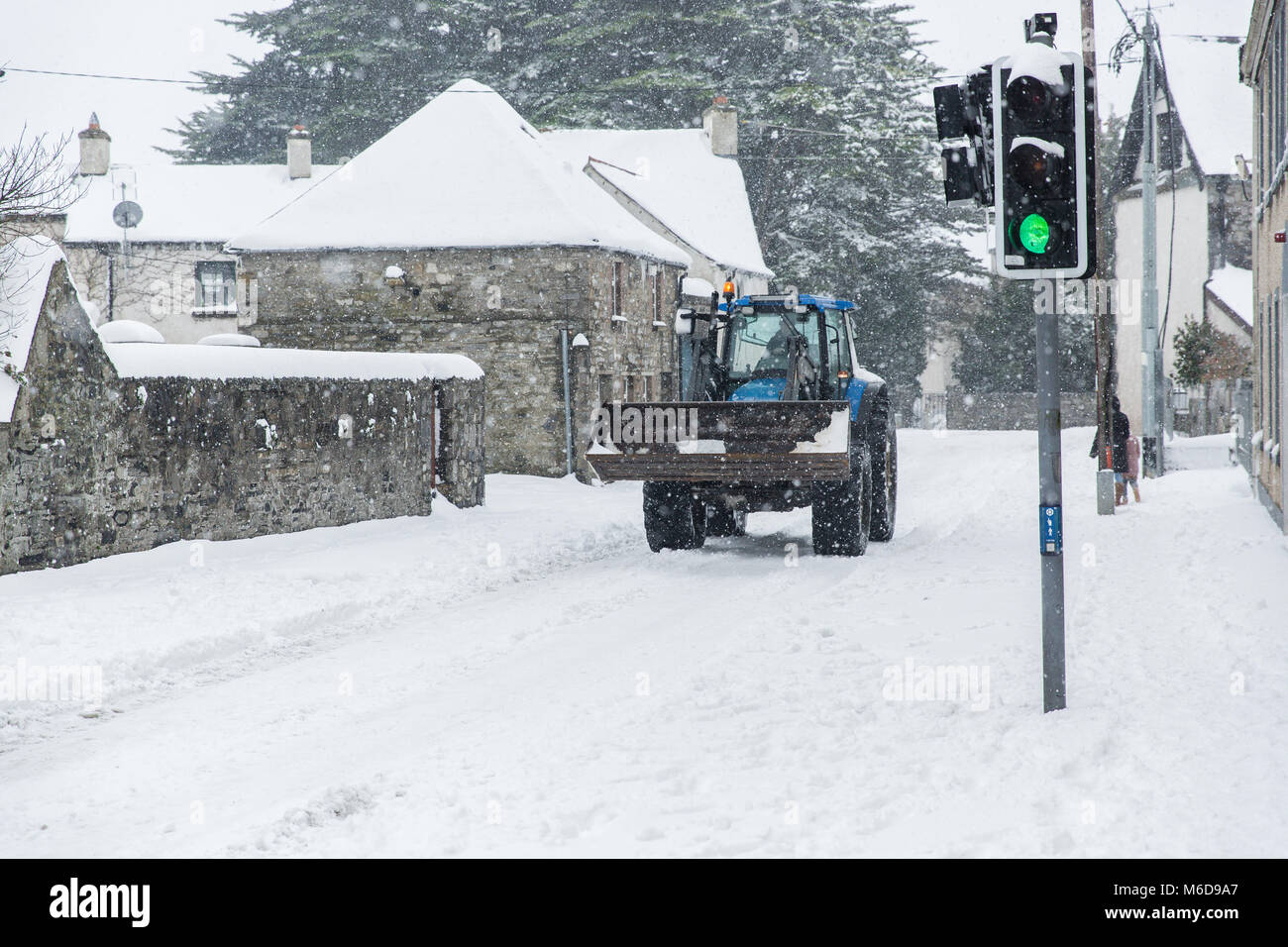 Celbridge, Kildare, Irland. 02 Mär 2018: Traktor mit Frontlader fahren durch im Schnee Celbridge abgedeckt. Die Bauern werden mobilisiert, um zu helfen, die Straßen als Gemeinderäte Kampf mit der Menge an Schnee fallen durch kalte Welle' Beat aus dem Osten' brachte, gefolgt von Sturm Emma fertig zu löschen. Stockfoto
