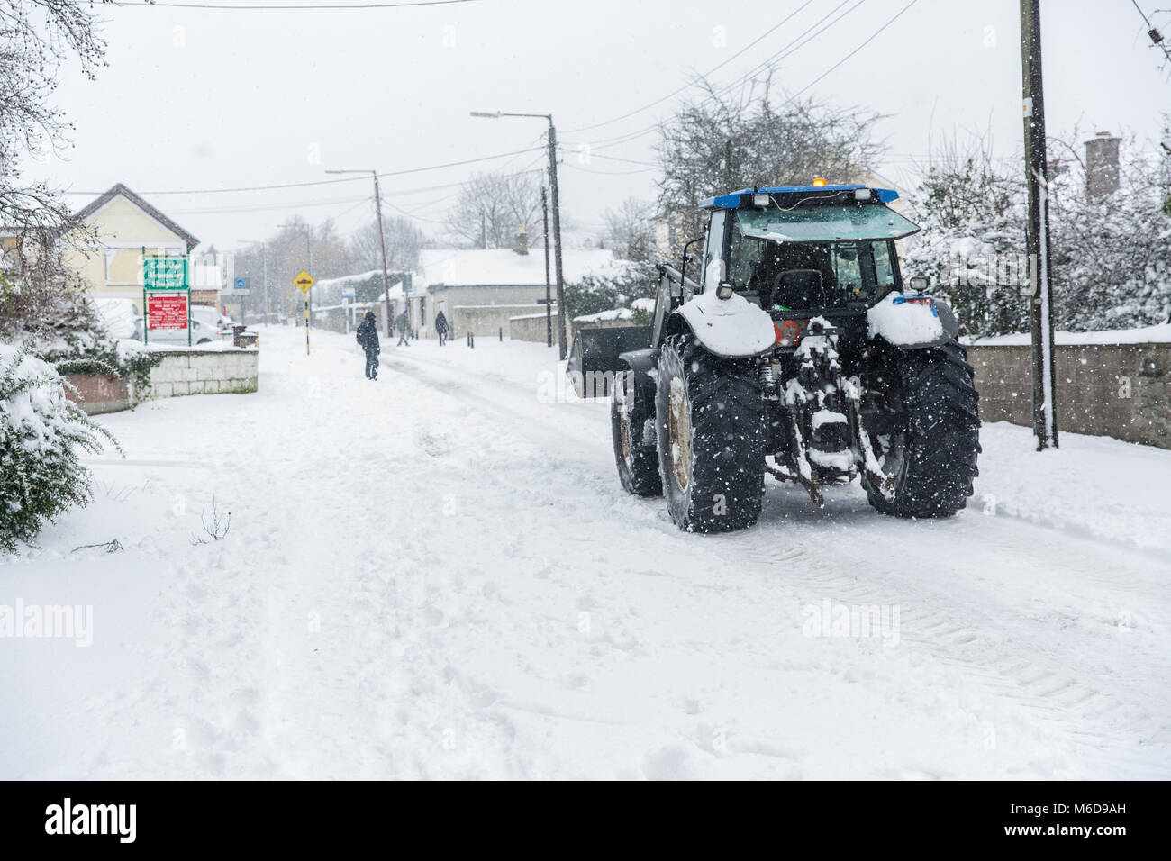 Celbridge, Kildare, Irland. 02 Mär 2018: Traktor mit Frontlader fahren durch im Schnee Celbridge abgedeckt. Die Bauern werden mobilisiert, um zu helfen, die Straßen als Gemeinderäte Kampf mit der Menge an Schnee fallen durch kalte Welle' Beat aus dem Osten' brachte, gefolgt von Sturm Emma fertig zu löschen. Stockfoto