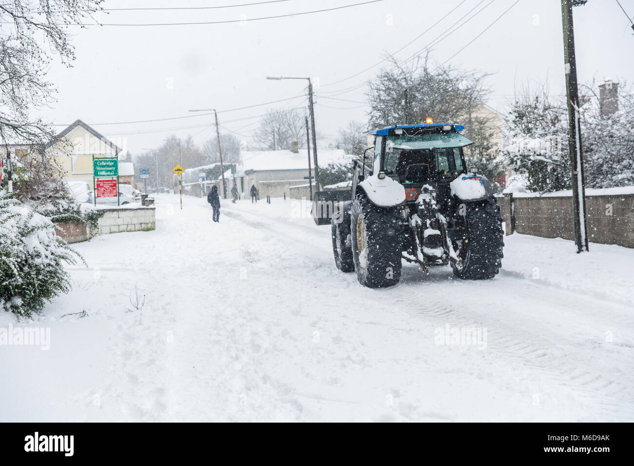 Celbridge, Kildare, Irland. 02 Mär 2018: Traktor mit Frontlader fahren durch im Schnee Celbridge abgedeckt. Die Bauern werden mobilisiert, um zu helfen, die Straßen als Gemeinderäte Kampf mit der Menge an Schnee fallen durch kalte Welle' Beat aus dem Osten' brachte, gefolgt von Sturm Emma fertig zu löschen. Stockfoto