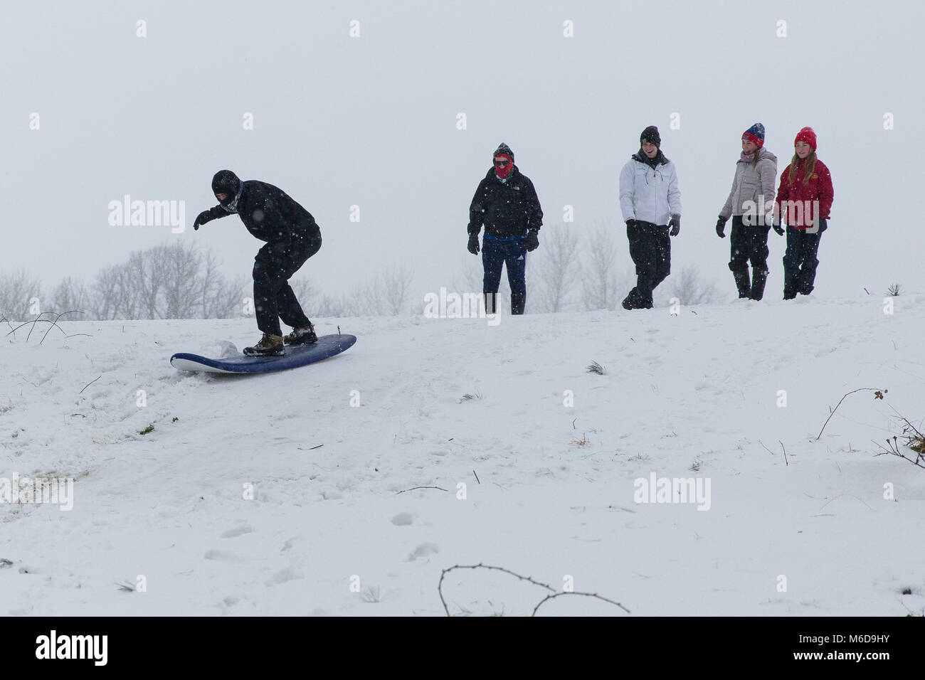 Celbridge, Kildare, Irland. 02 Mär 2018: Jugendliche mit Surf Board nach unten zu schieben Sie die Hügel mit Schnee bedeckt. Tier aus dem Osten durch Sturm Emma gefolgt brachte mehr Schnee und starke Winde in ganz Irland. Stockfoto