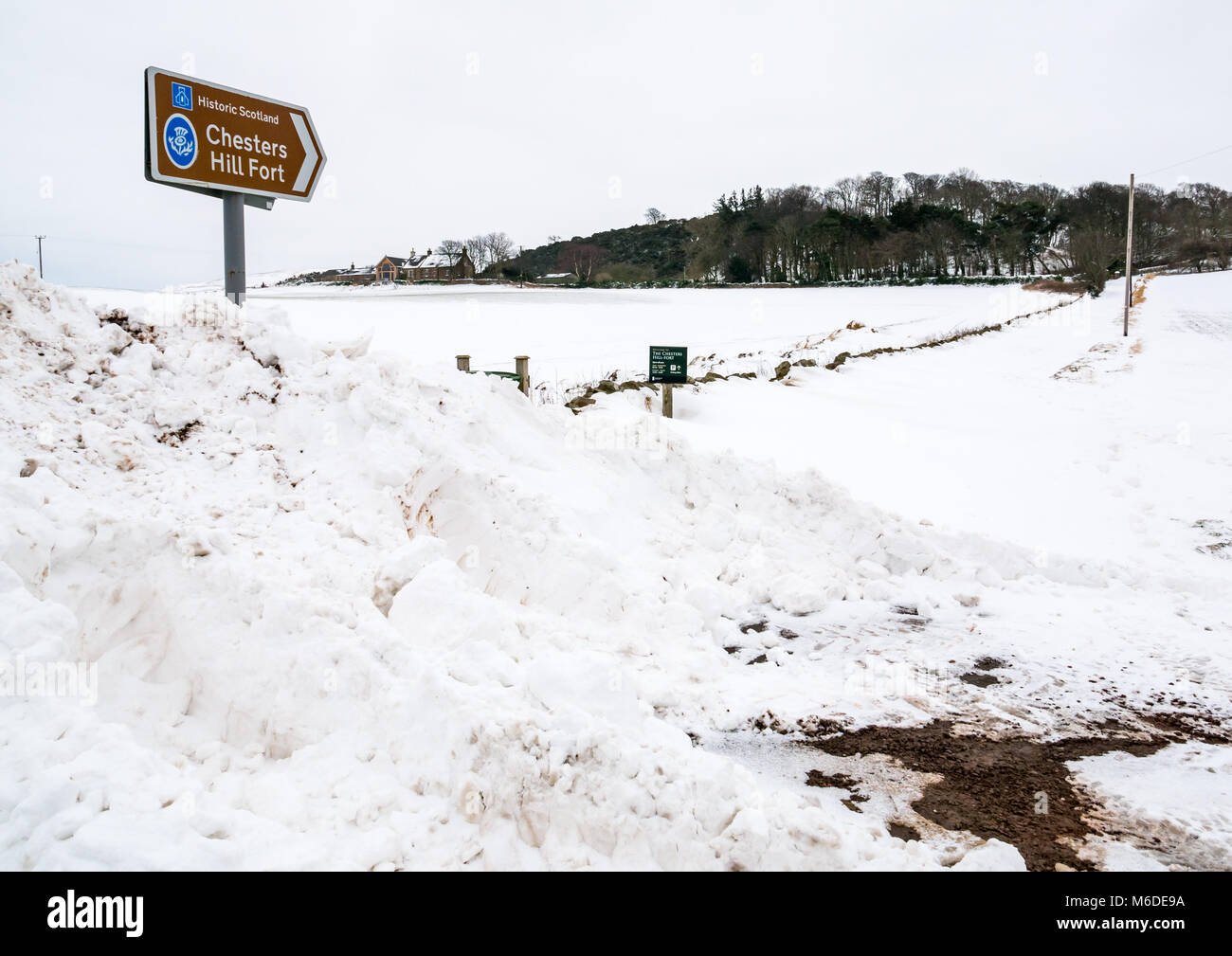 East Lothian, Schottland, Großbritannien, 3. März 2018. Wetter in Großbritannien: Nach dem extremen arktischen Wetterereignis mit dem Spitznamen „das Biest aus dem Osten“ wird eine lokale Straße durch riesige Schneeverwehungen gesperrt. Ein historisches Schottland-Schild weist den Weg zum Chesters Hill Fort mit der Straße, die von einer Schneeverwehung bedeckt ist Stockfoto