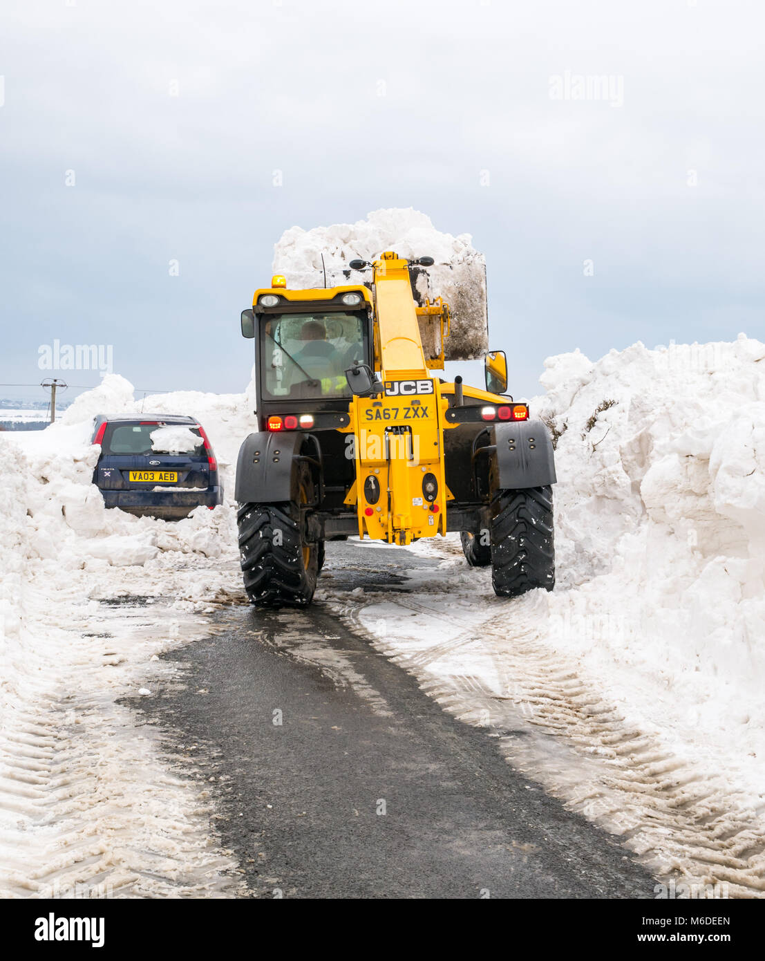 East Lothian, Schottland, Vereinigtes Königreich, 3. März 2018. UK Wetter: Die lokale Straße zwischen Drem und Haddington wird durch große Schneeverwehungen geschlossen, nachdem die extremen arktischen Wetter event Spitznamen "das Tier aus dem Osten". Ein Rat digger ist das Löschen der Straße. Ein Auto ist im Schnee begraben Stockfoto