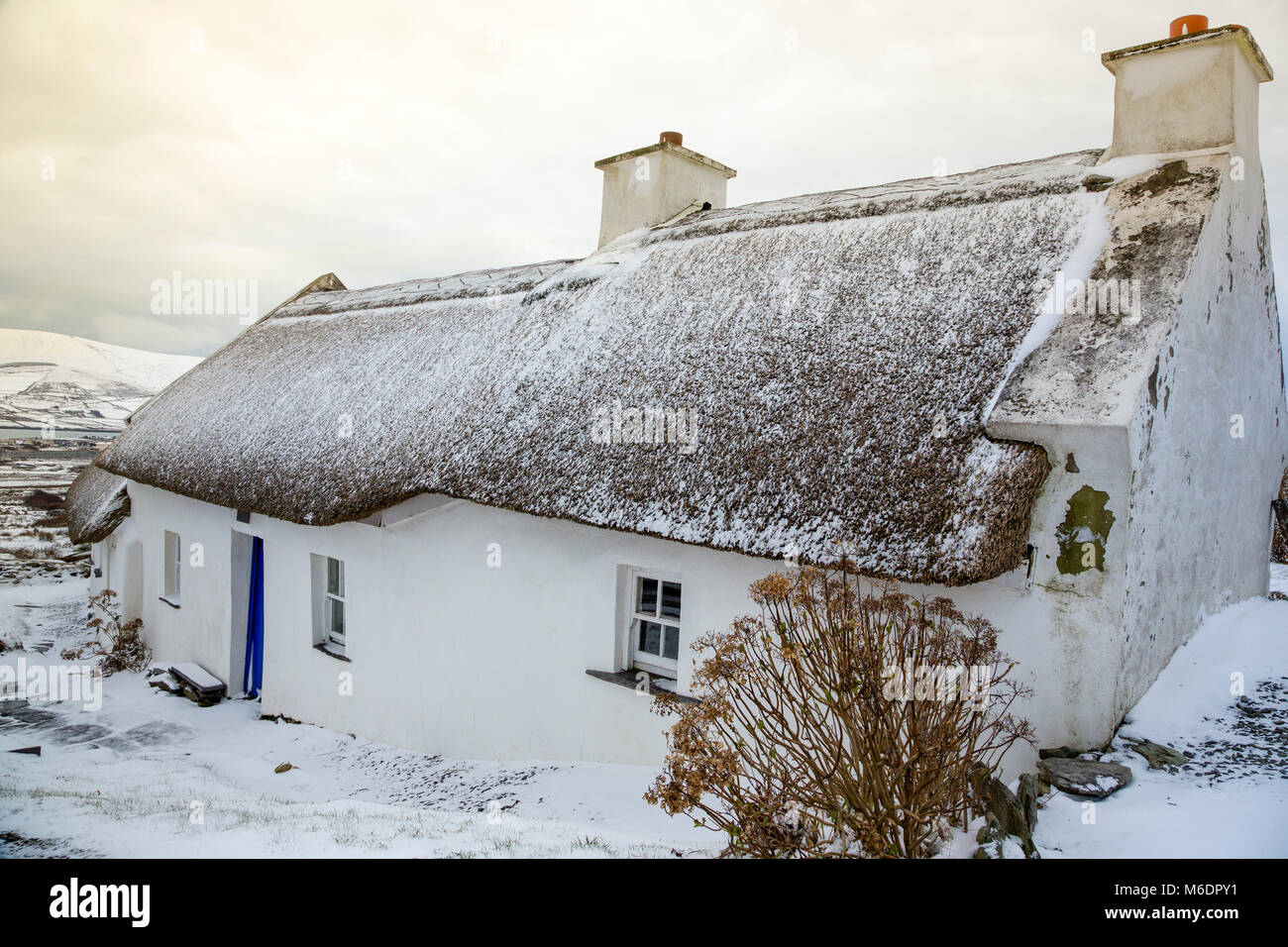 Schnee bedeckt strohgedeckten Irish cottage in country lane auf Valentia Island, County Kerry, Irland Stockfoto