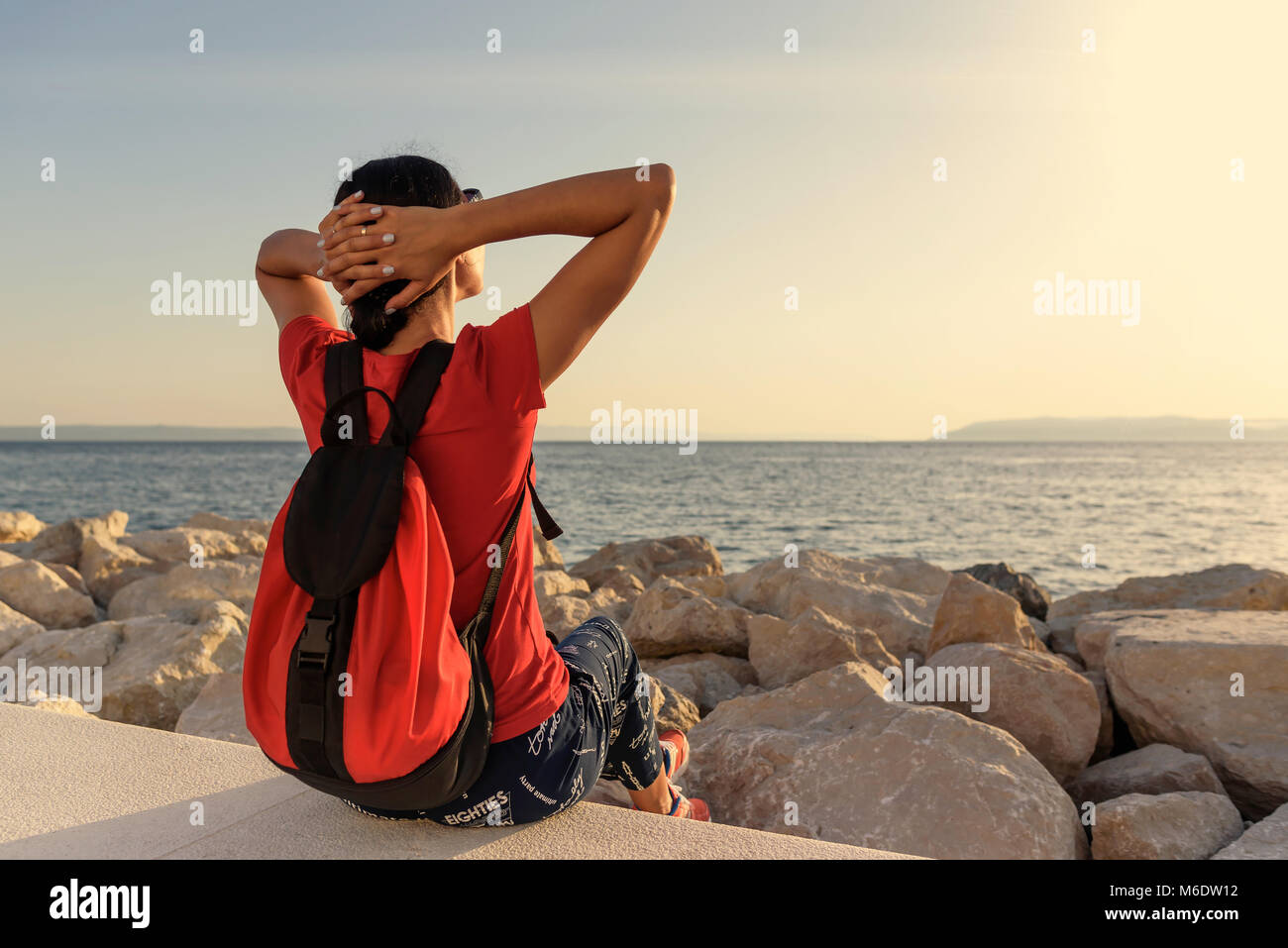 Frau sieht den Sonnenuntergang, sitzen auf einem betonpfeiler. Stockfoto