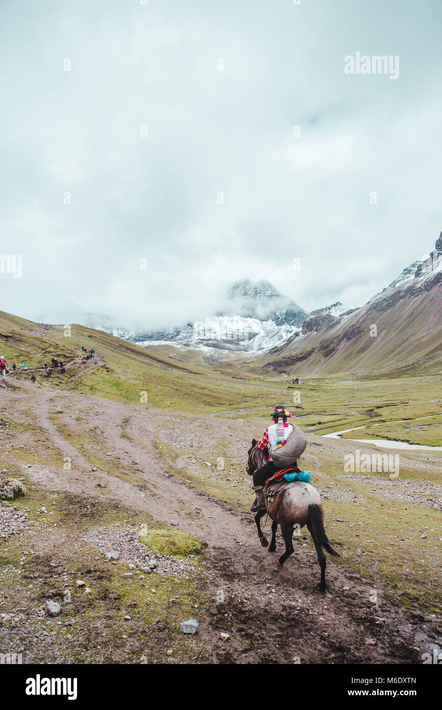 Die traditionellen indigenen Quechua Reiter reitet sein Pferd in die Täler der Region Cusco in Peru, neben Regenbogen-berg Stockfoto