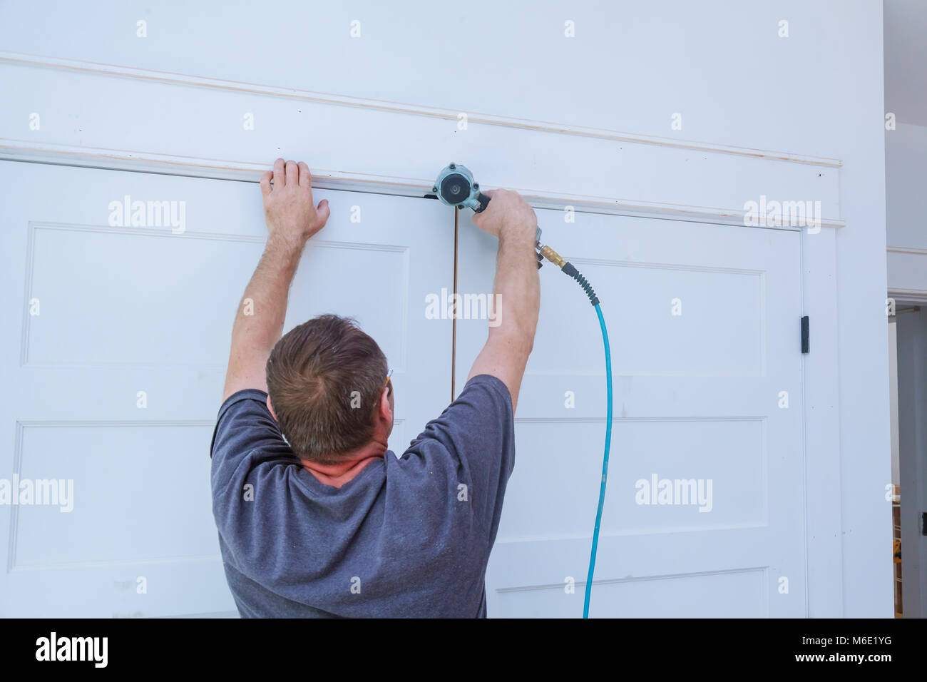 Tischler mit Brad Nagel Pistole an Formteile auf Türen, framing trim mit dem Warnhinweis, die alle Elektrowerkzeuge auf sie gezeigt haben zur Veranschaulichung Sicherheit c Stockfoto