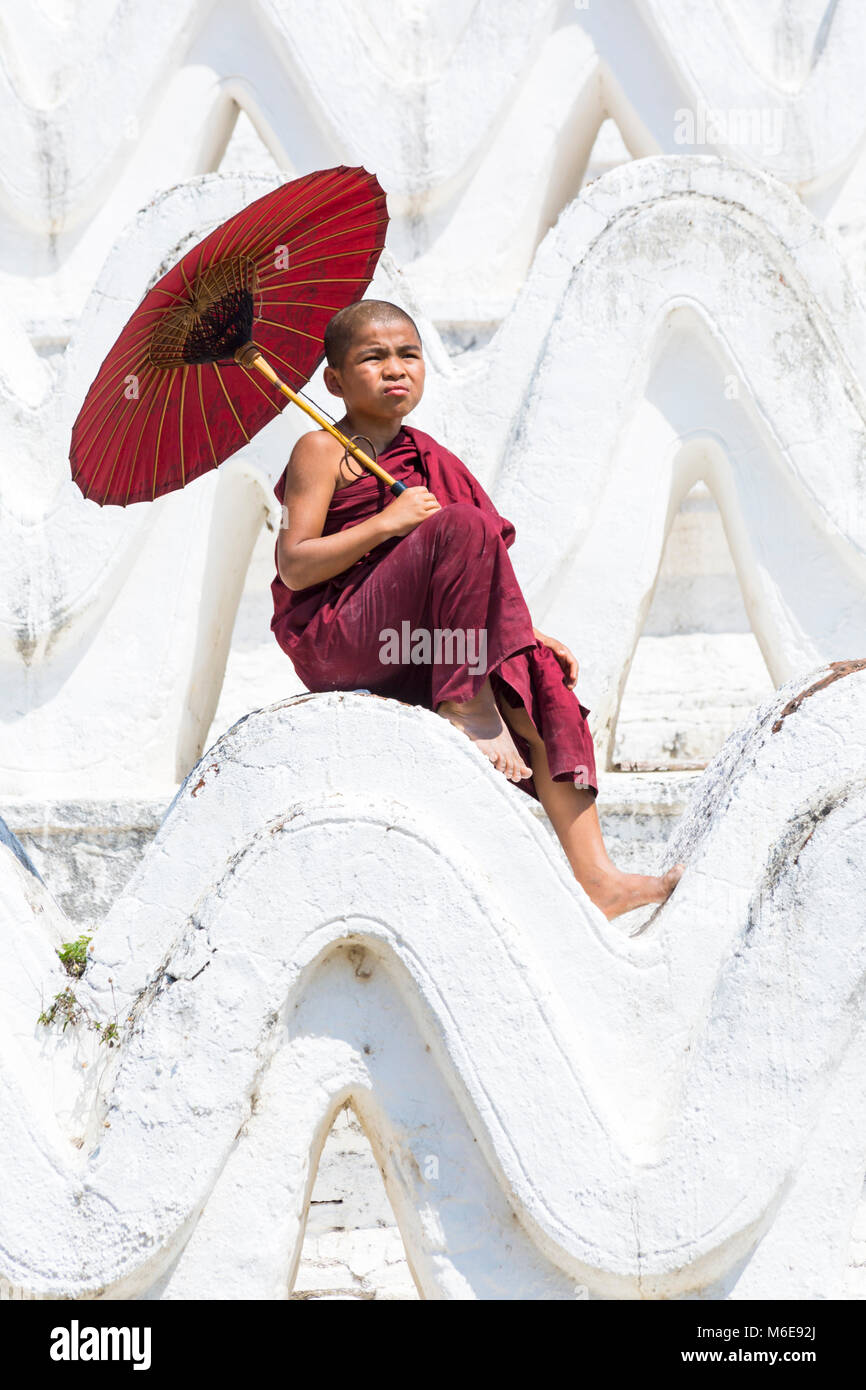 Junge Novizin buddhistischer Mönch sitzt Holding Sonnenschirm am Myatheindan Pagode (auch als Hsinbyume Pagode bekannt), Mingun, Myanmar (Burma), Asien im Februar Stockfoto