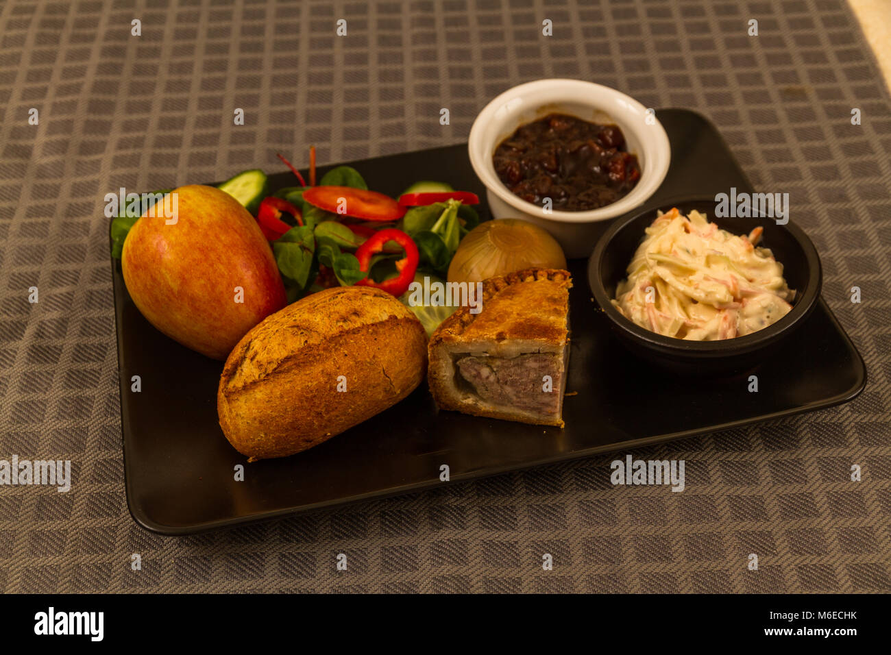 Pflüger's Mittagessen mit Pork Pie, Gurke, eingelegte Zwiebeln, Salat, Krautsalat und Brot, und Apple. Stockfoto
